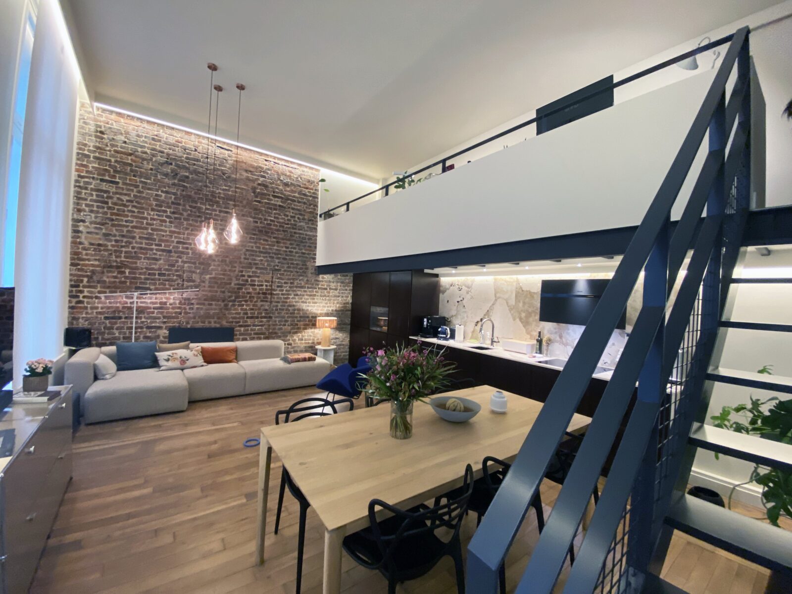 Loft en brique décapée avec mezzanine et escalier métallique noir, table en chêne, Paris IX