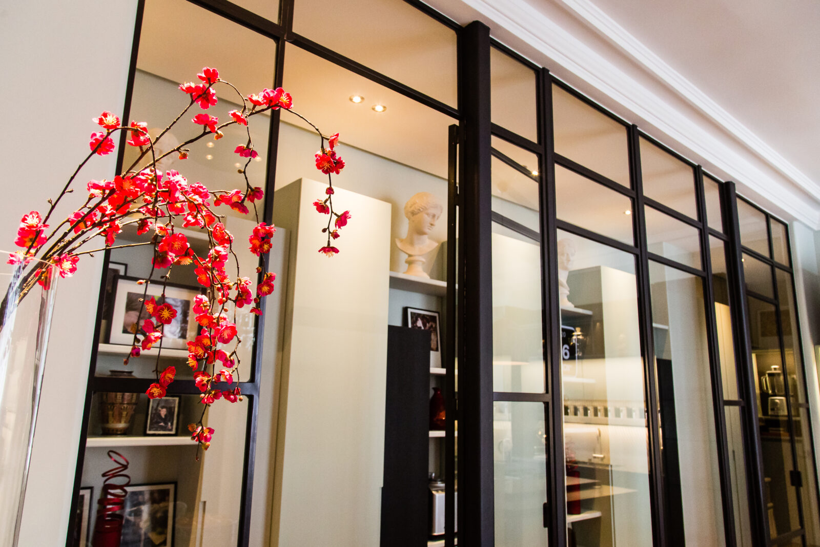 Verrière métallique et rangements blancs de la galerie d'entrée, fleurs rouges, Paris XVII