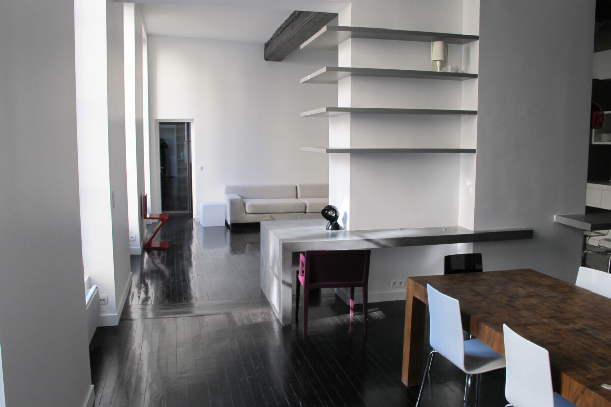 Loft blanc au parquet teinté noir, étagères murales et table à manger sombre, atelier devenu loft Paris II