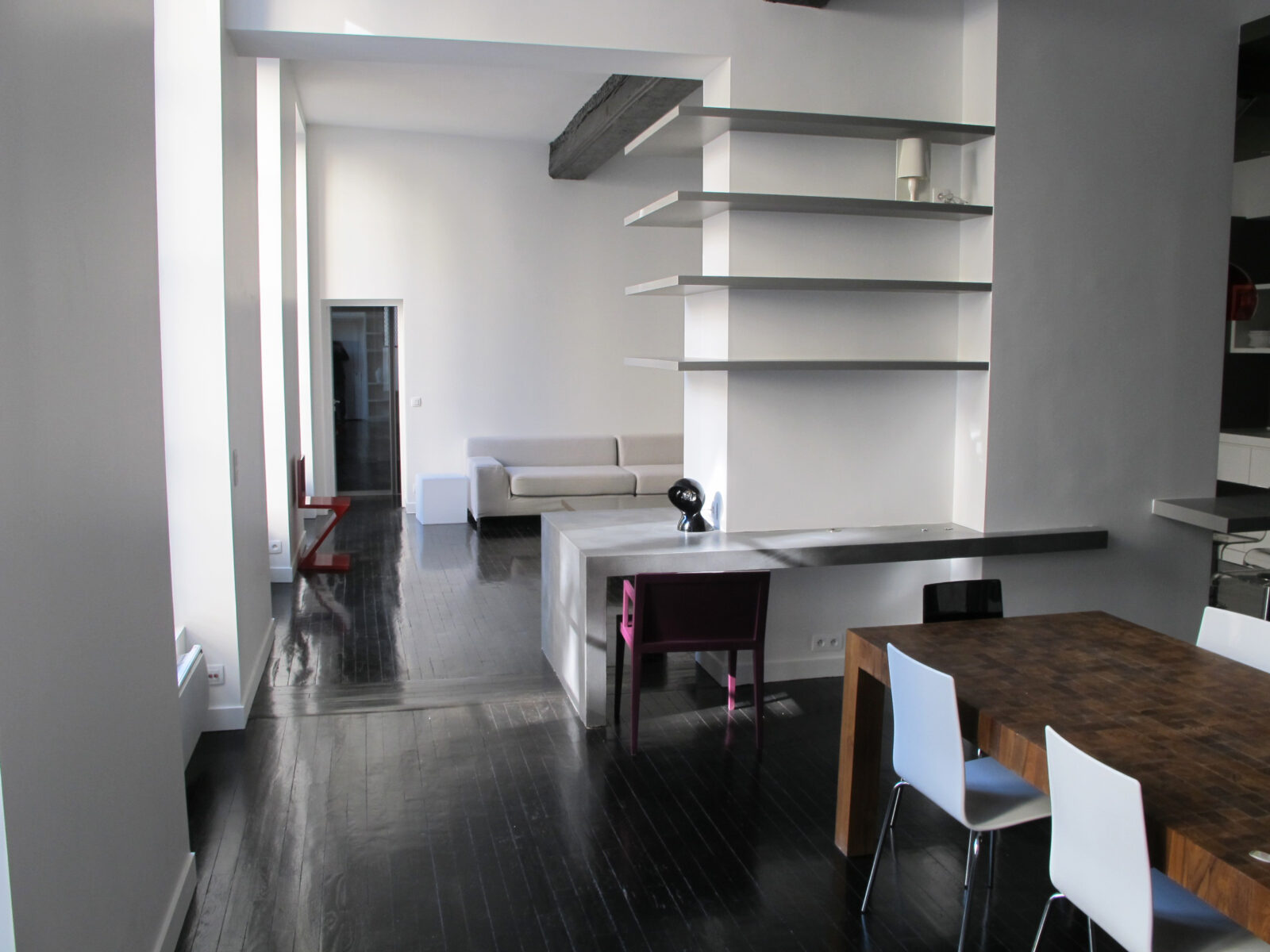 Loft blanc au parquet teinté noir, étagères murales et table à manger sombre, atelier devenu loft Paris II