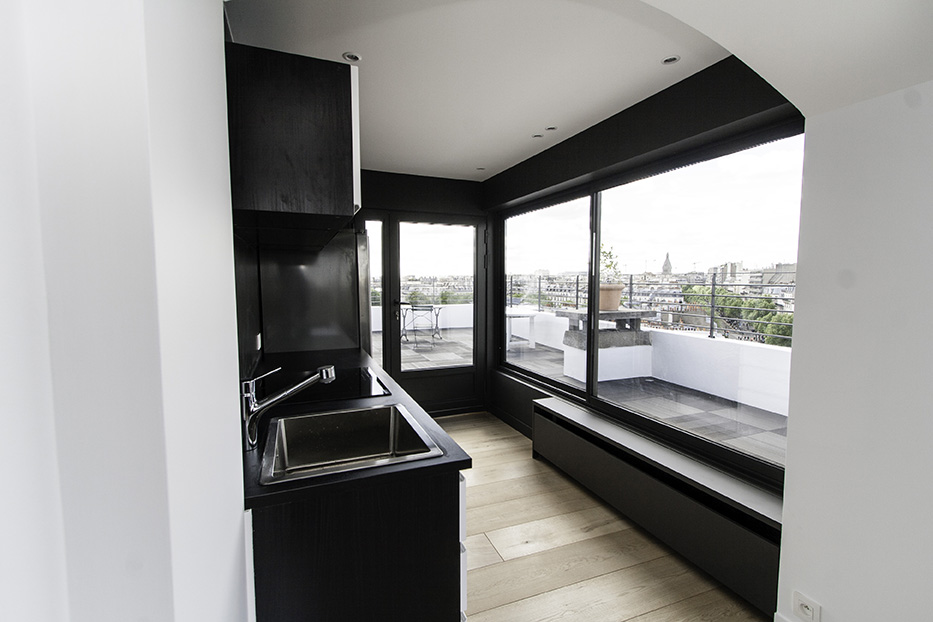 Kitchenette noire et baie vitrée donnant sur la terrasse
